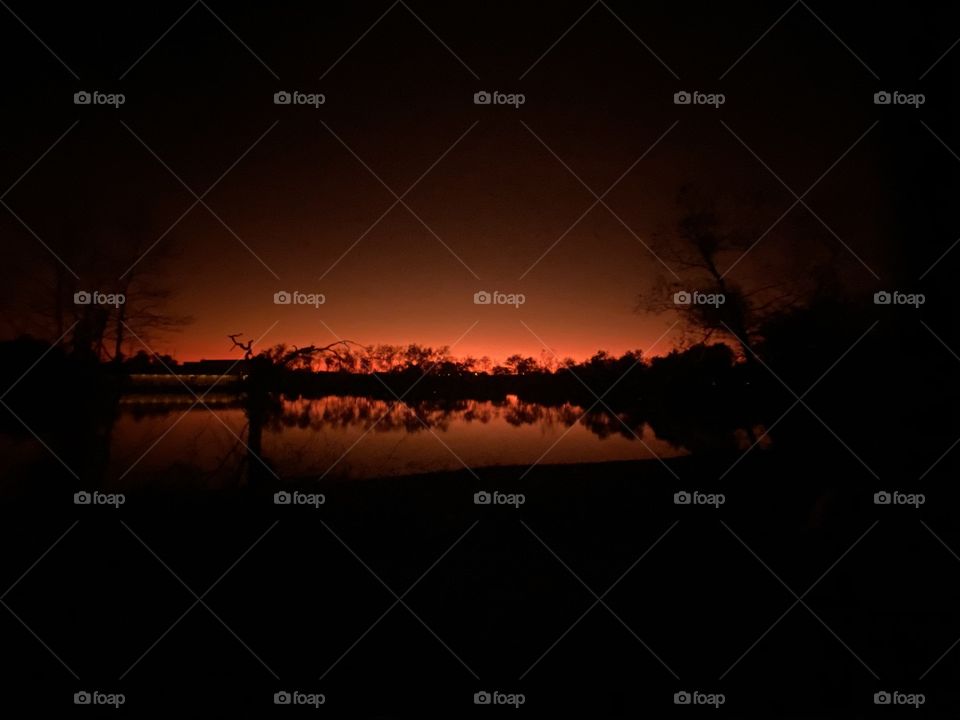 Reflections of shore line composure in comparison to Colorful Backlit Glow illuminating Lake Waters, Trees and Shrubs. 