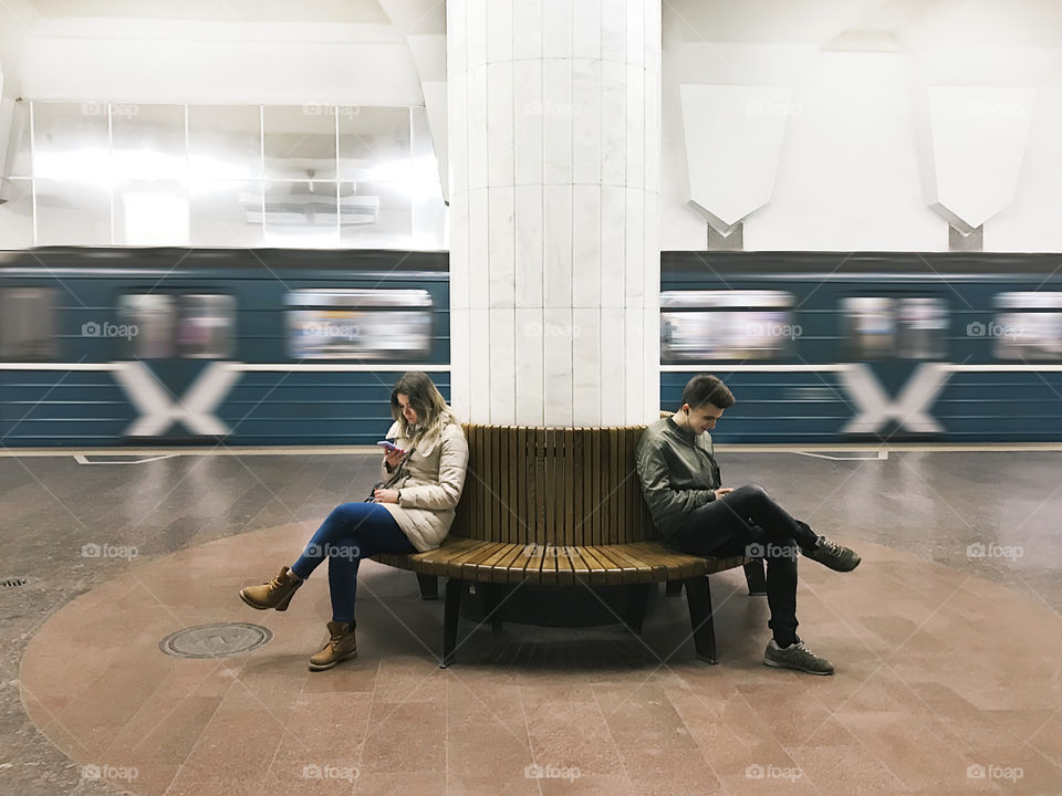 Young woman and young man using mobile phone at subway station 