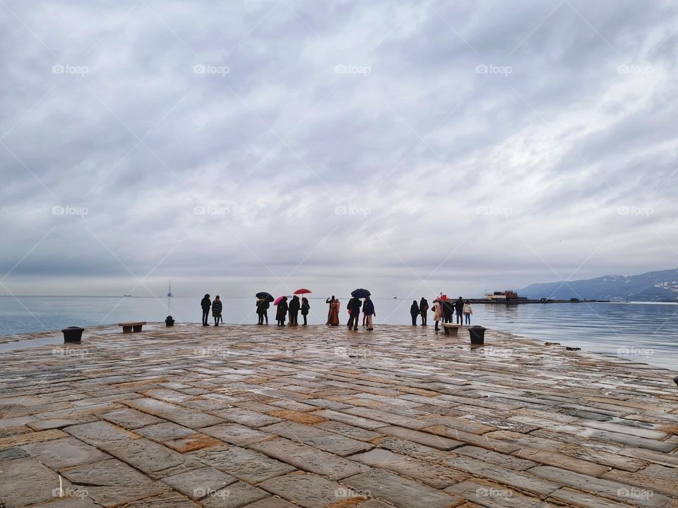 group of people with open umbrellas stand on the pier and look at the sea