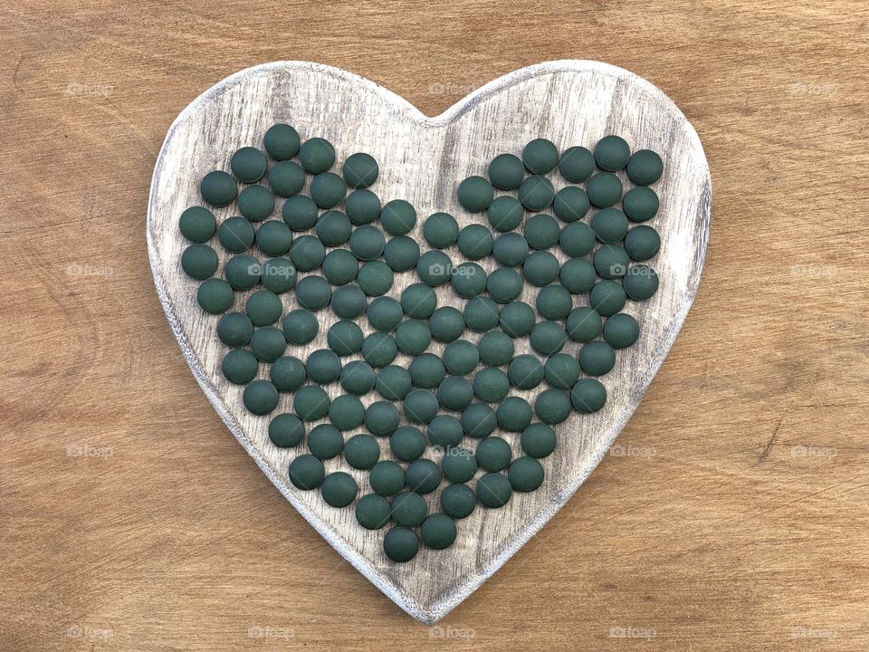 Spirulina pills on a wooden heart