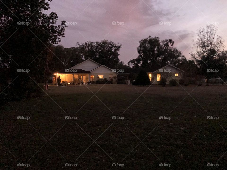 Country scene of warmly lit houses in soft dusk twilight against a purplish sky like a Thomas Kinkaid painting 