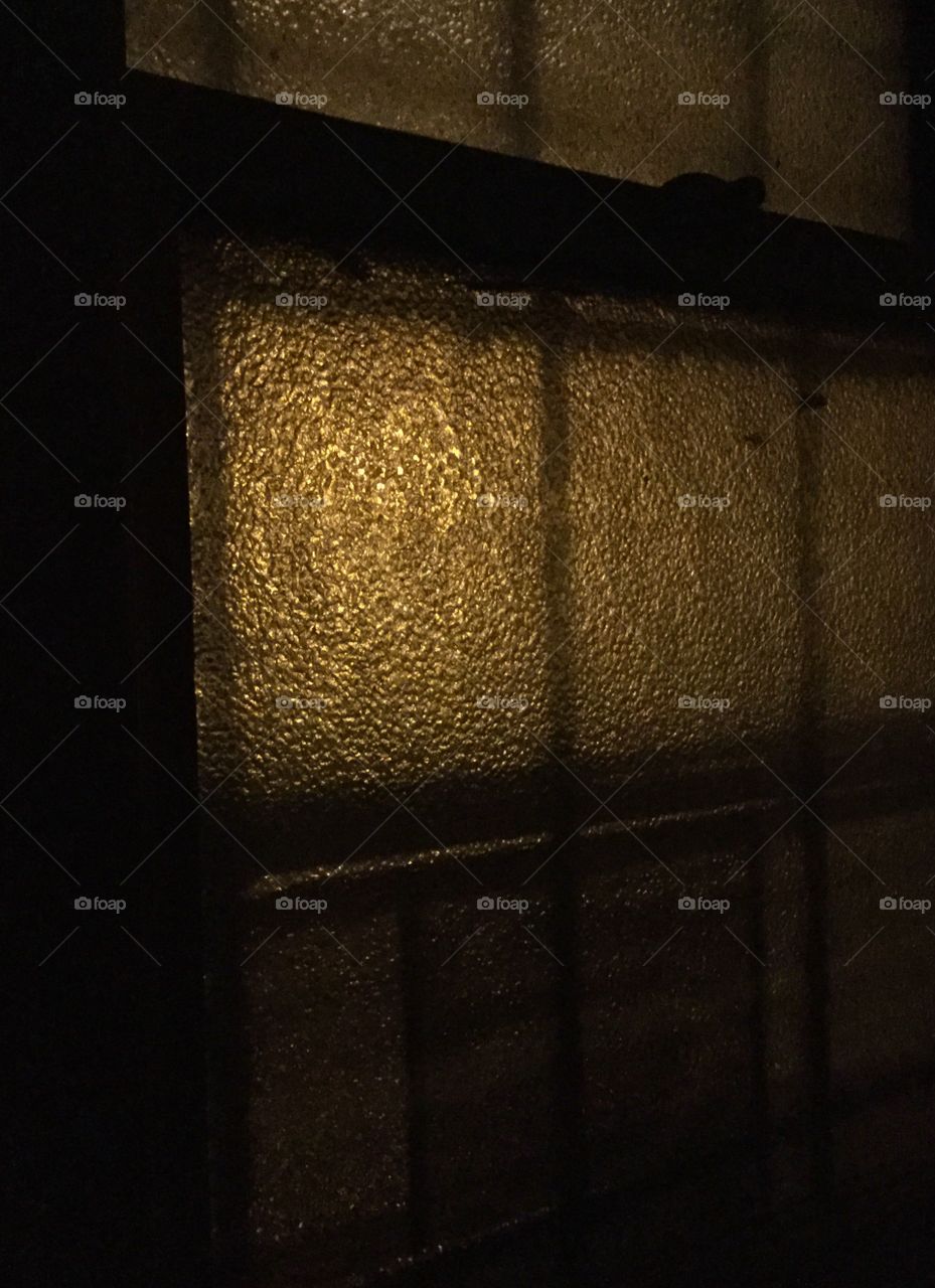 Interior textured glass window at night. Golden exterior light. Strong contrasting shadows.