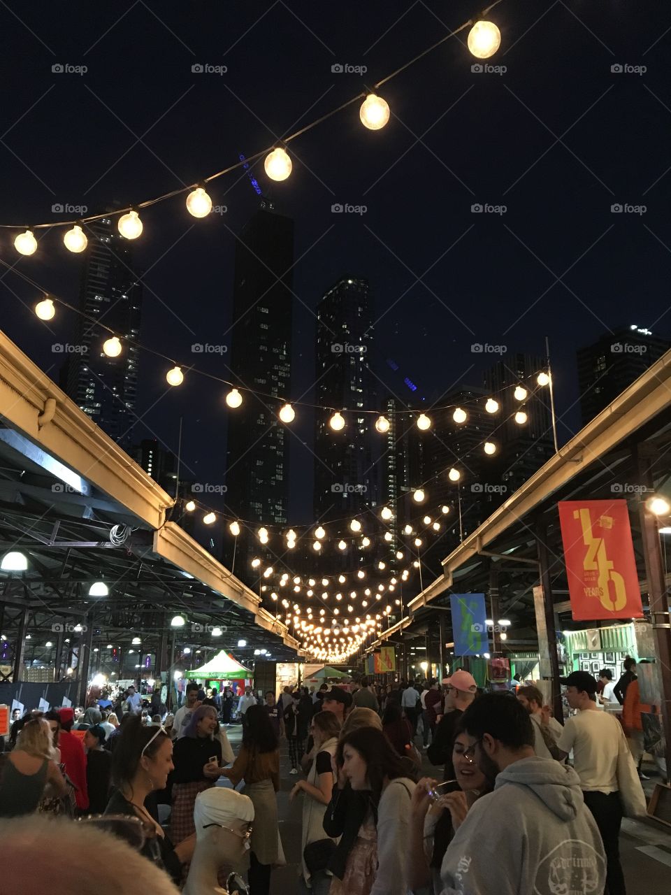 Melbourne Market with dotted lights and the city landscape in the background. Excellent food, flowers and fun on offer. 