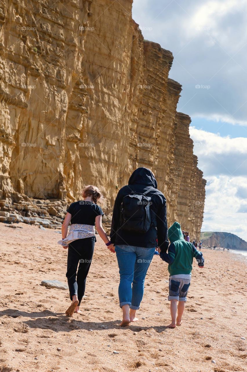 Family walking on golden beach underneath towering cliffs on sunny summer day. Jurassic coastline of West Bay in Dorset. UK