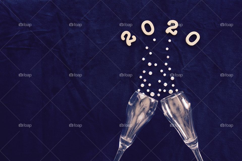 Flat lay of the numbers ‘2020’ above champagne glasses with rhinestone bubbles on classic blue background - copy space on left side of landscape format