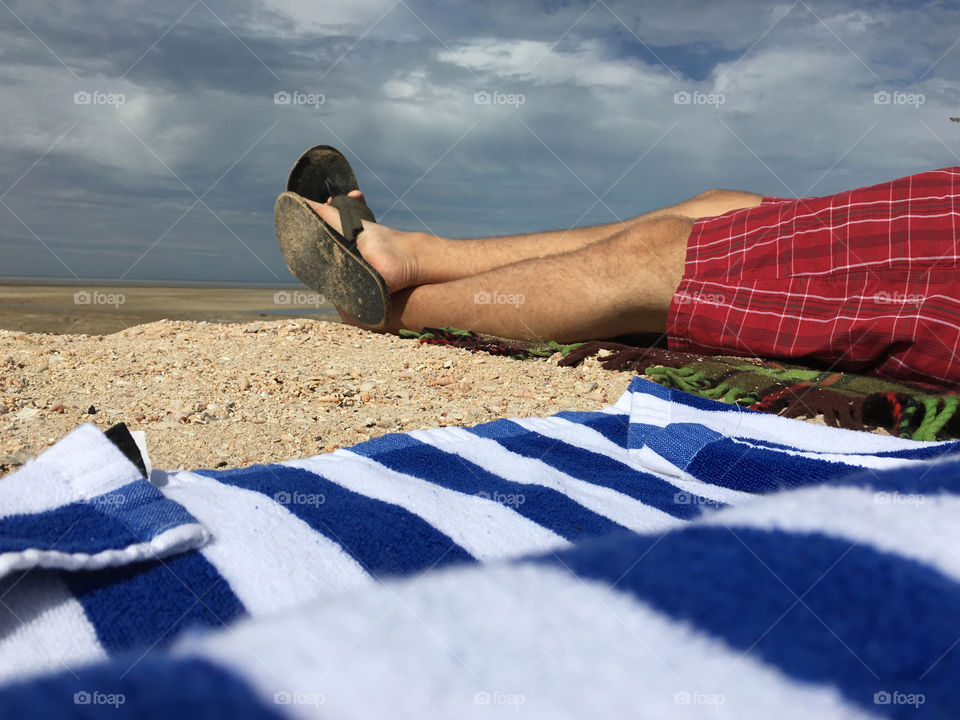 Man on beach in towel relaxing and wearing red plaid shorts and sandals