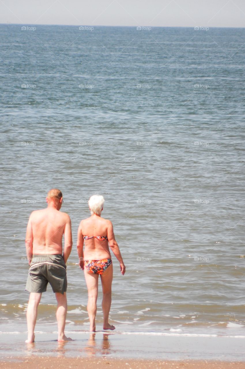 A older couple walking towards the sea, enjoying their free time
