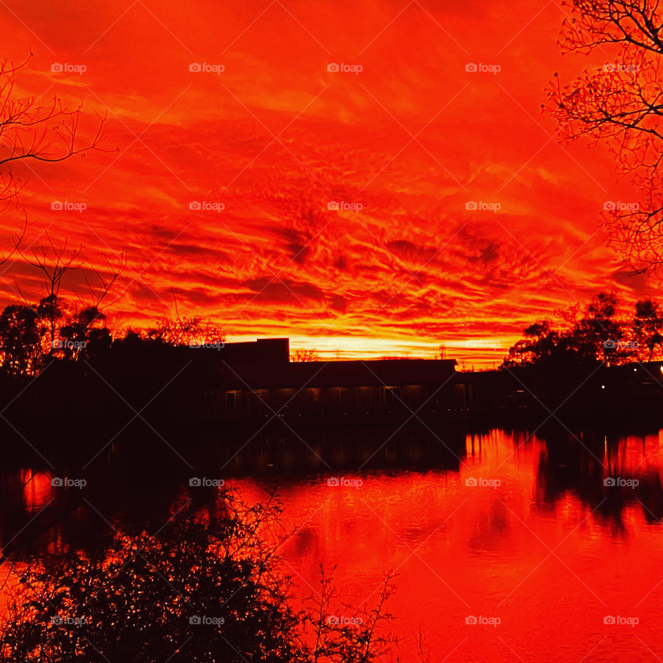 Fiery orange blaze unbelievable sunset-Twilight. Lake water reflections from orange Blaze. Shore reflections on Water. 