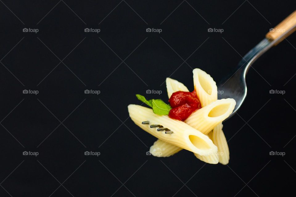 Fork with spaghetti and tomato sauce on black background 