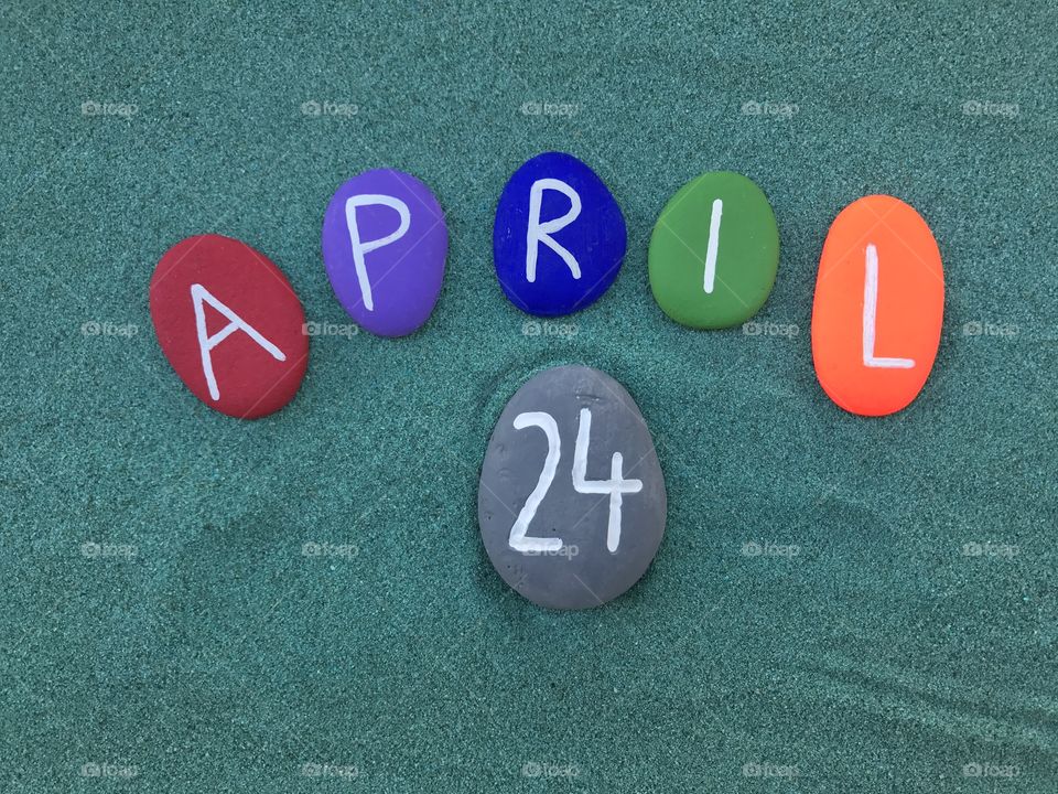 24  April, calendar date with colored stones over green sand 