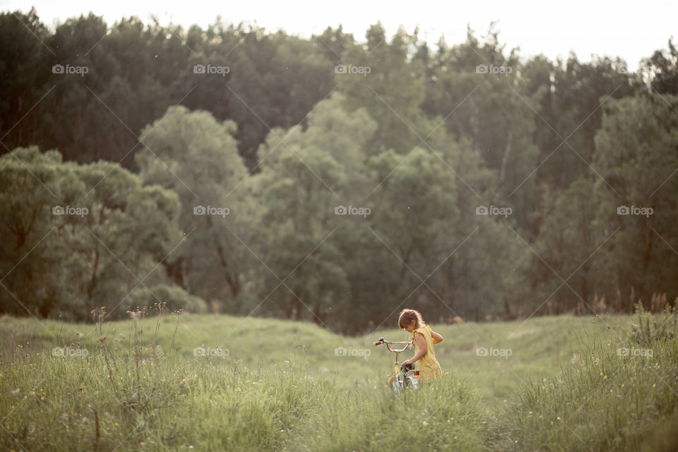 Little girl with bicycle in the summer field 