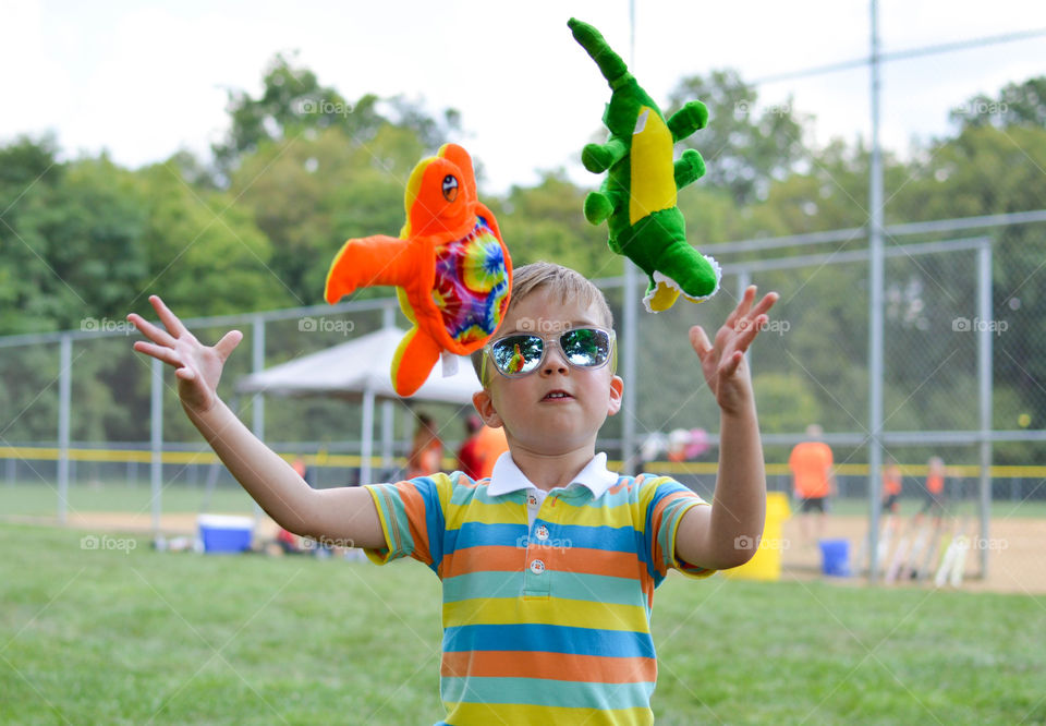 Young boy juggling two stuffed animals outdoors