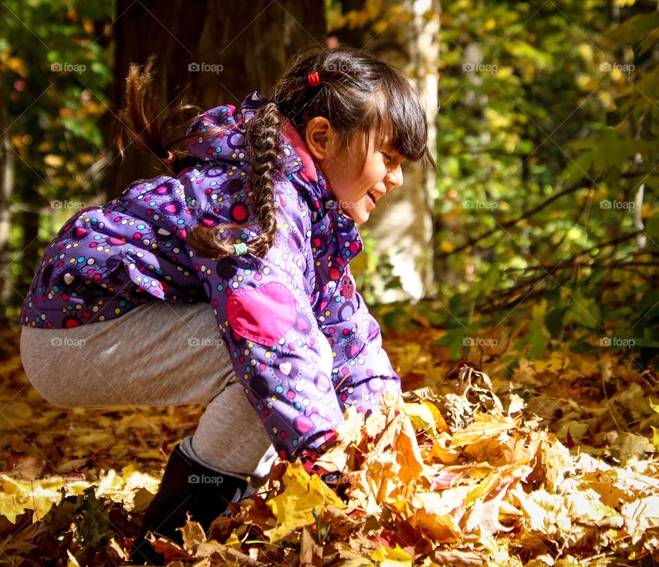 Cute girl in a colorful jacket is playing with fallen leaves