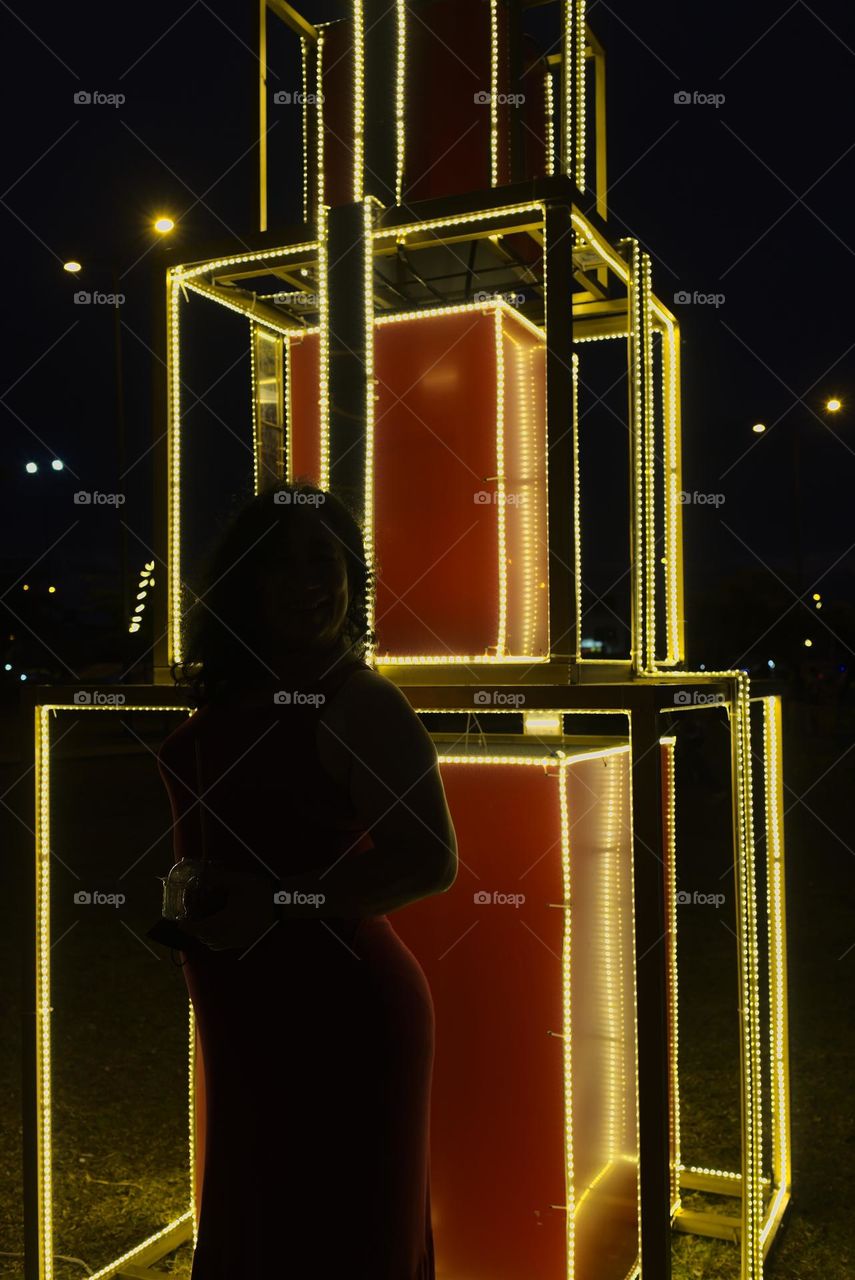 Silhouette of woman next to giant Christmas gift in city park