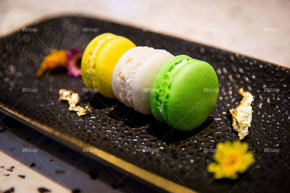 Sweet delicious yellow green and white macaroon cookies on a black plate