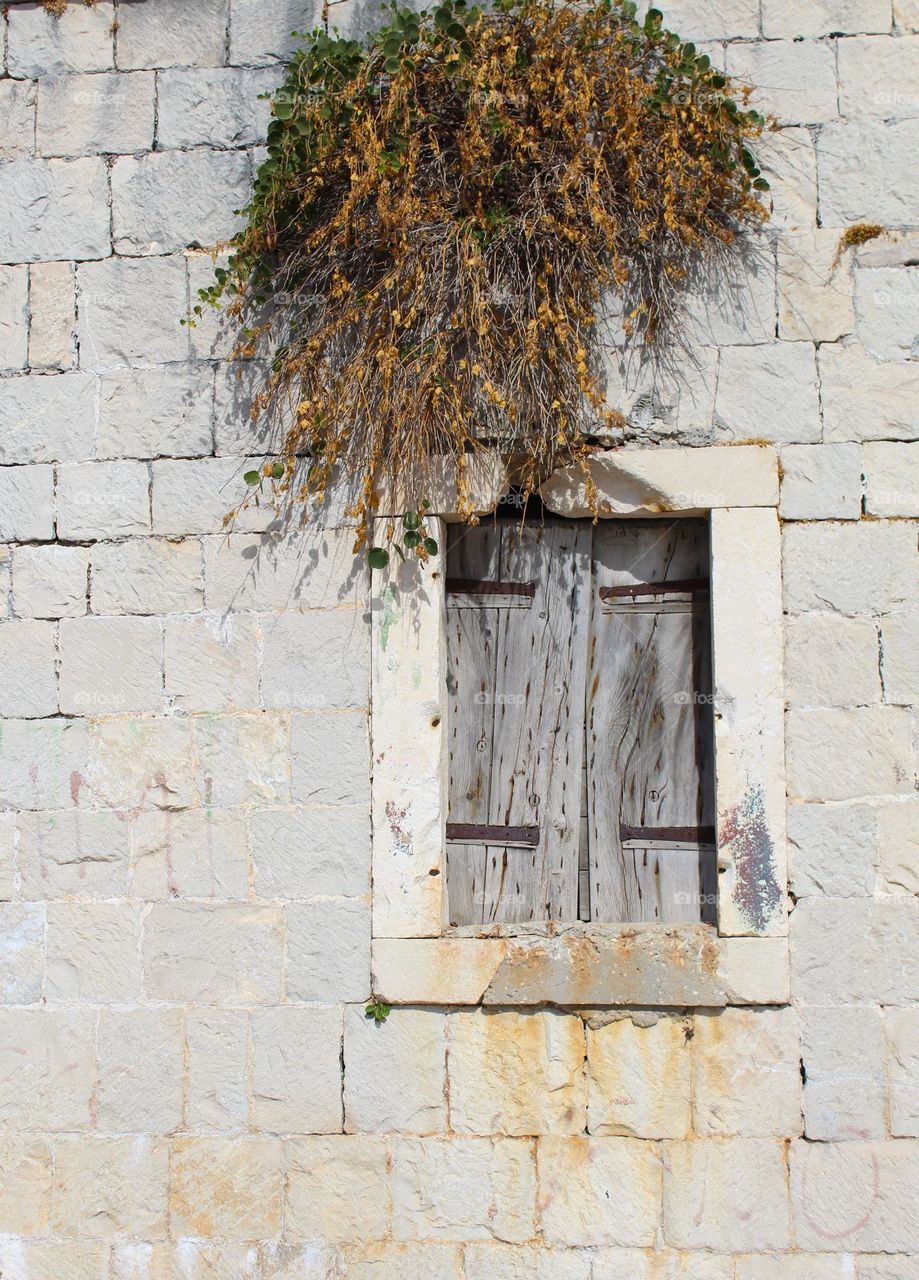 Old wooden window with metal hinges on a stone wall