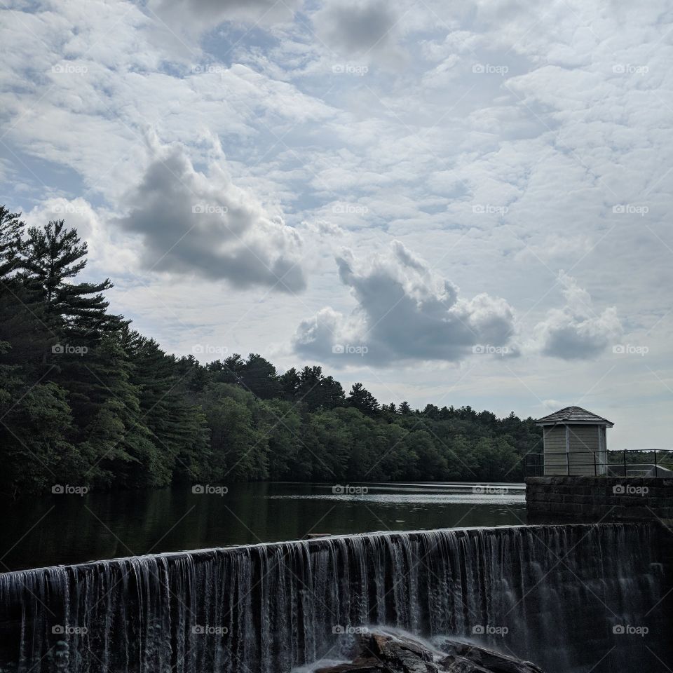 the reservoir waterfall with beautiful sky, clouds and thick trees in the background.