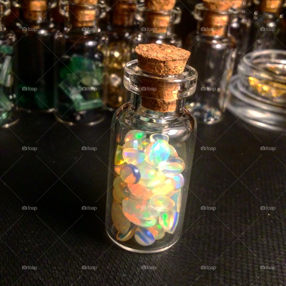 mini glass bottle full of different sized and shaped Ethiopian opal in front of other genomes in glass containers.
