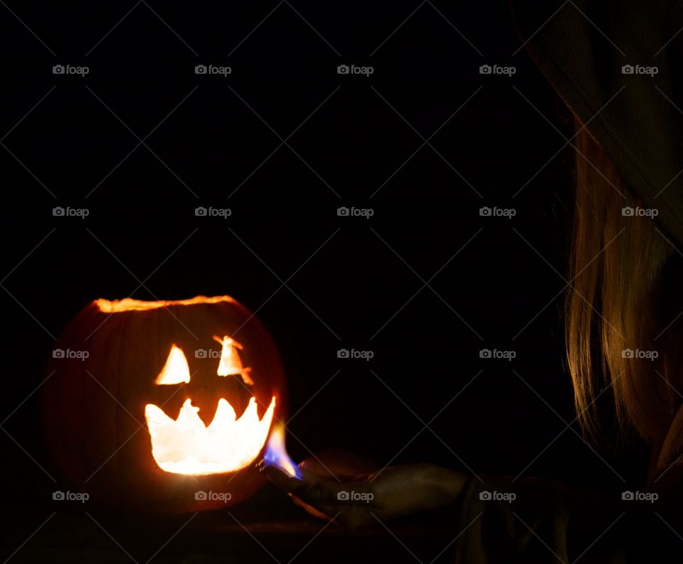 Lighting the Pumpkin; Woman using flame on finger tips to light pumpkin. 