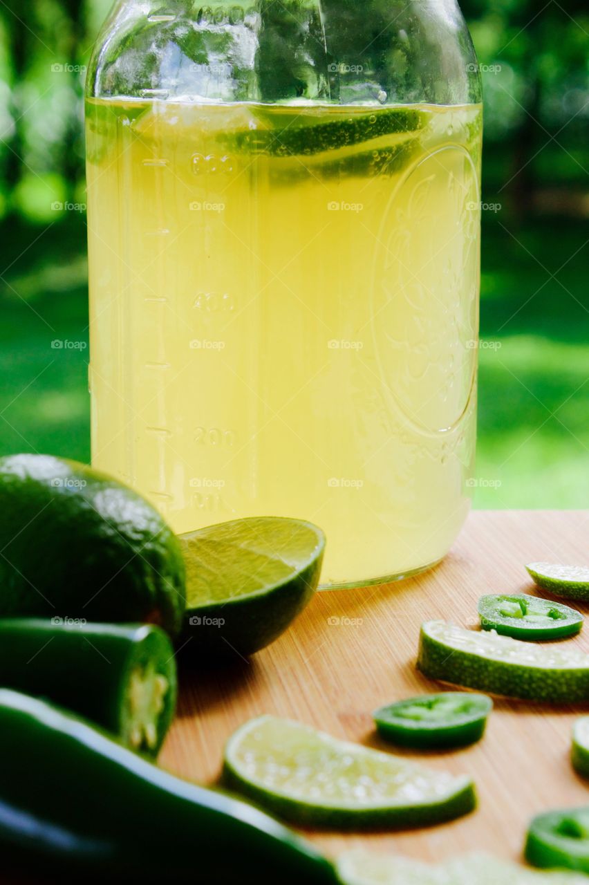 Refeshing lime-and-jalepeño-flavored kombucha, rebottled in a quart-size mason jar for a second ferment, with slices of lime and jalepeño on a bamboo cutting board, against a blurred outdoor background in summer