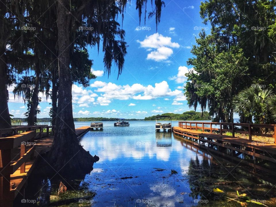 Canal with dock flowing into lake with boats under a blue sky with white clouds