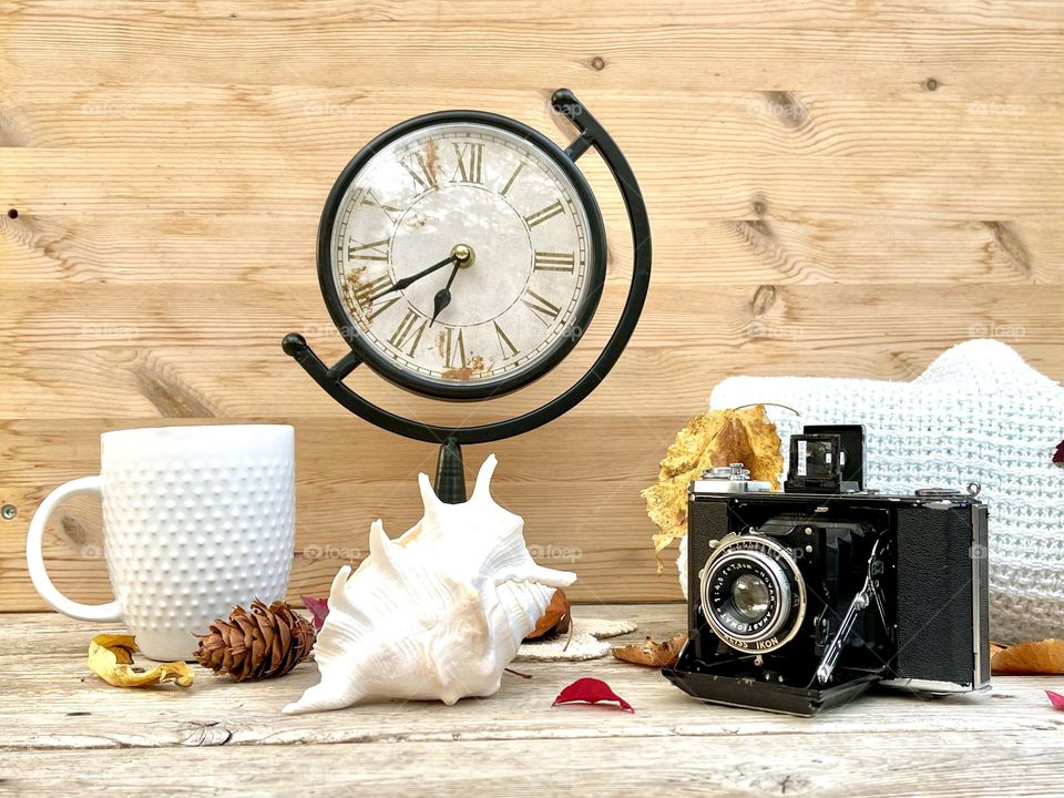 Autumn mood composition with old clock, photo camera, cup of tea, blanket 