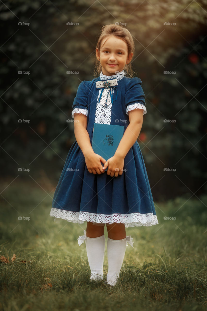 Little schoolgirl with a book at a park 