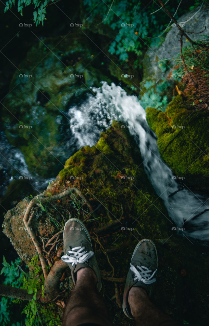 Man standing on top of a waterfall in the woods.