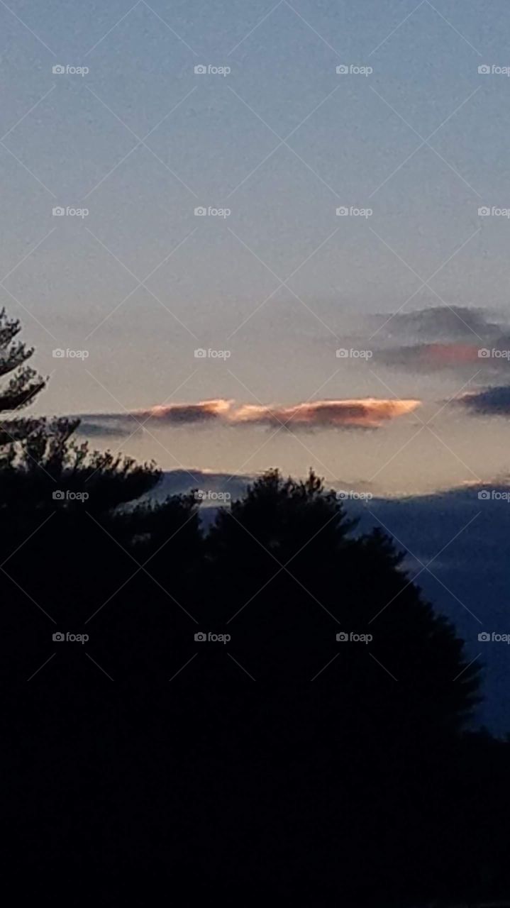 Sunrises & Sunsets of USA. Sunset over hills & treetops, all backlit. Delicate cloud formation is present.