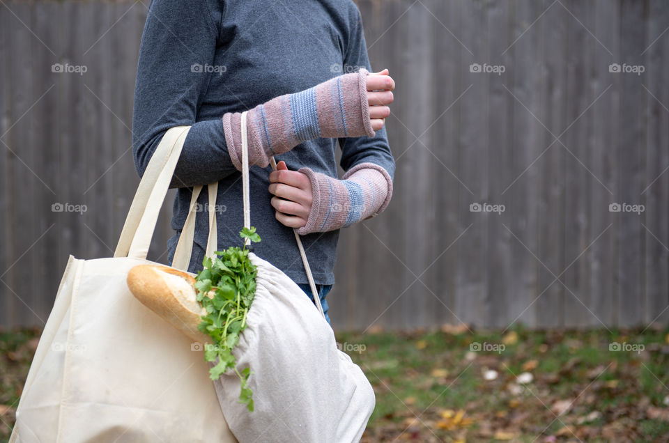 Person carrying fresh groceries in reusable bags outdoors