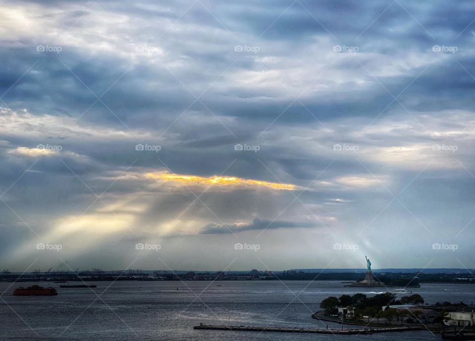 Sunlight breaking through clouds and shining on the Statue of Liberty in New York harbor 