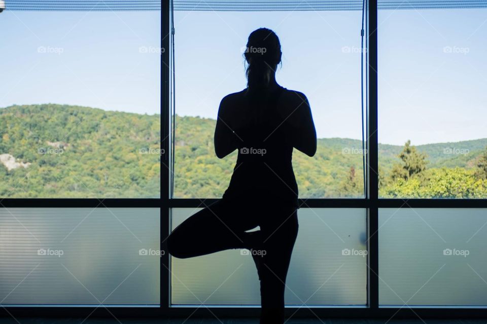 Young woman does a yoga session while looking out to a beautiful landscape of mountains 