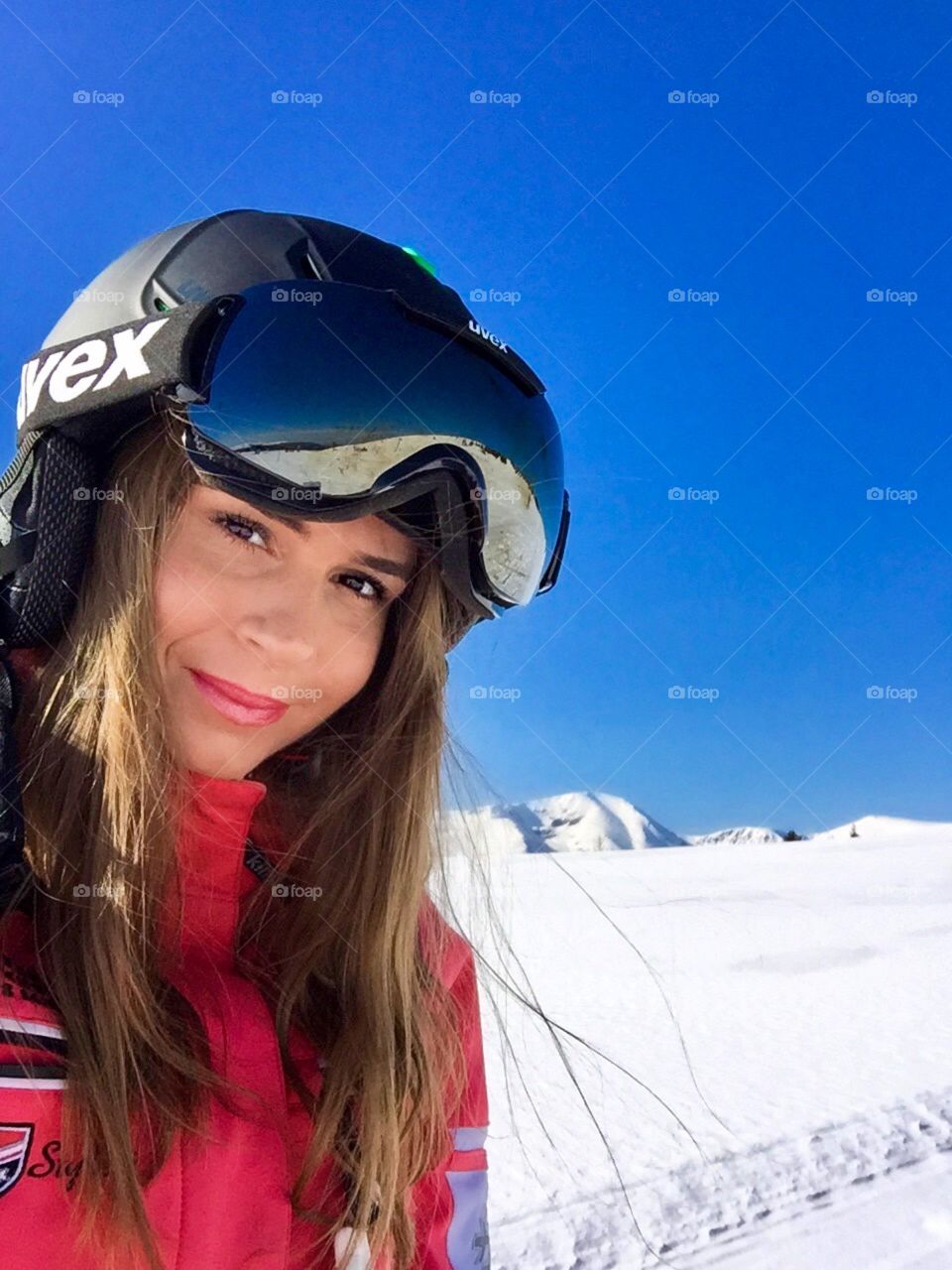 Portrait of woman with Uvex ski glasses and helmet with snowy mountains in the background