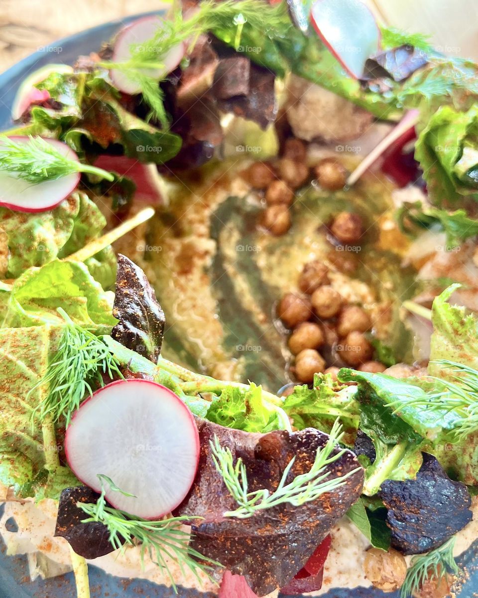 A colorful vegetarian plate with hummus, pickled veggies, chick peas, and  greens