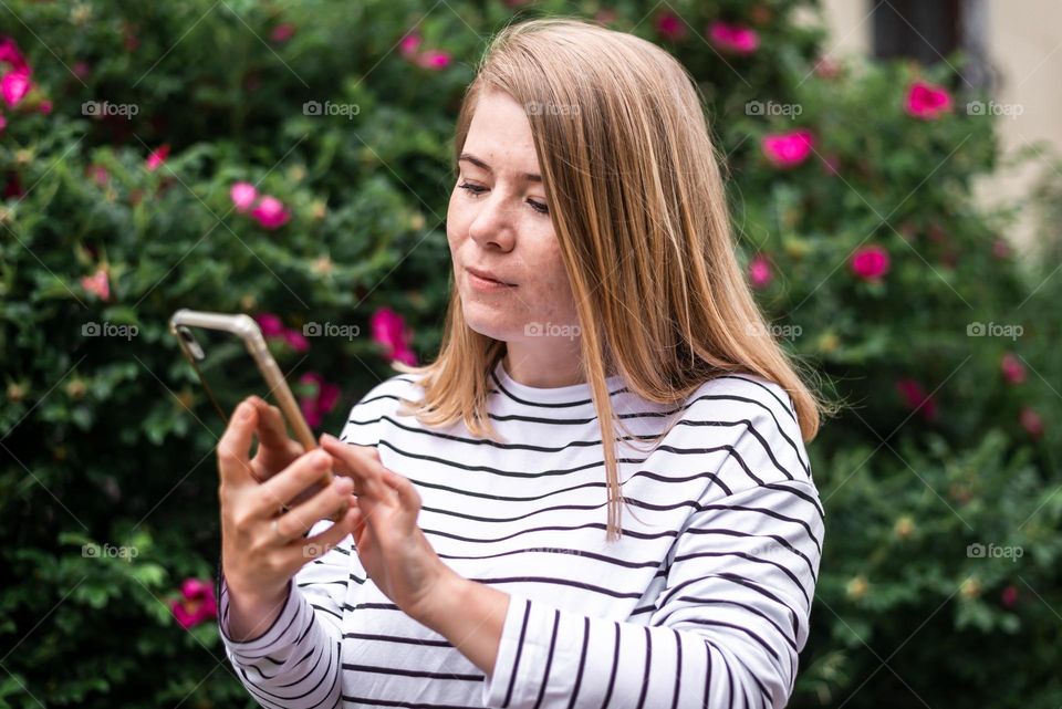 young beautiful girl in the park in spring holds a phone in her hands and takes a selfie