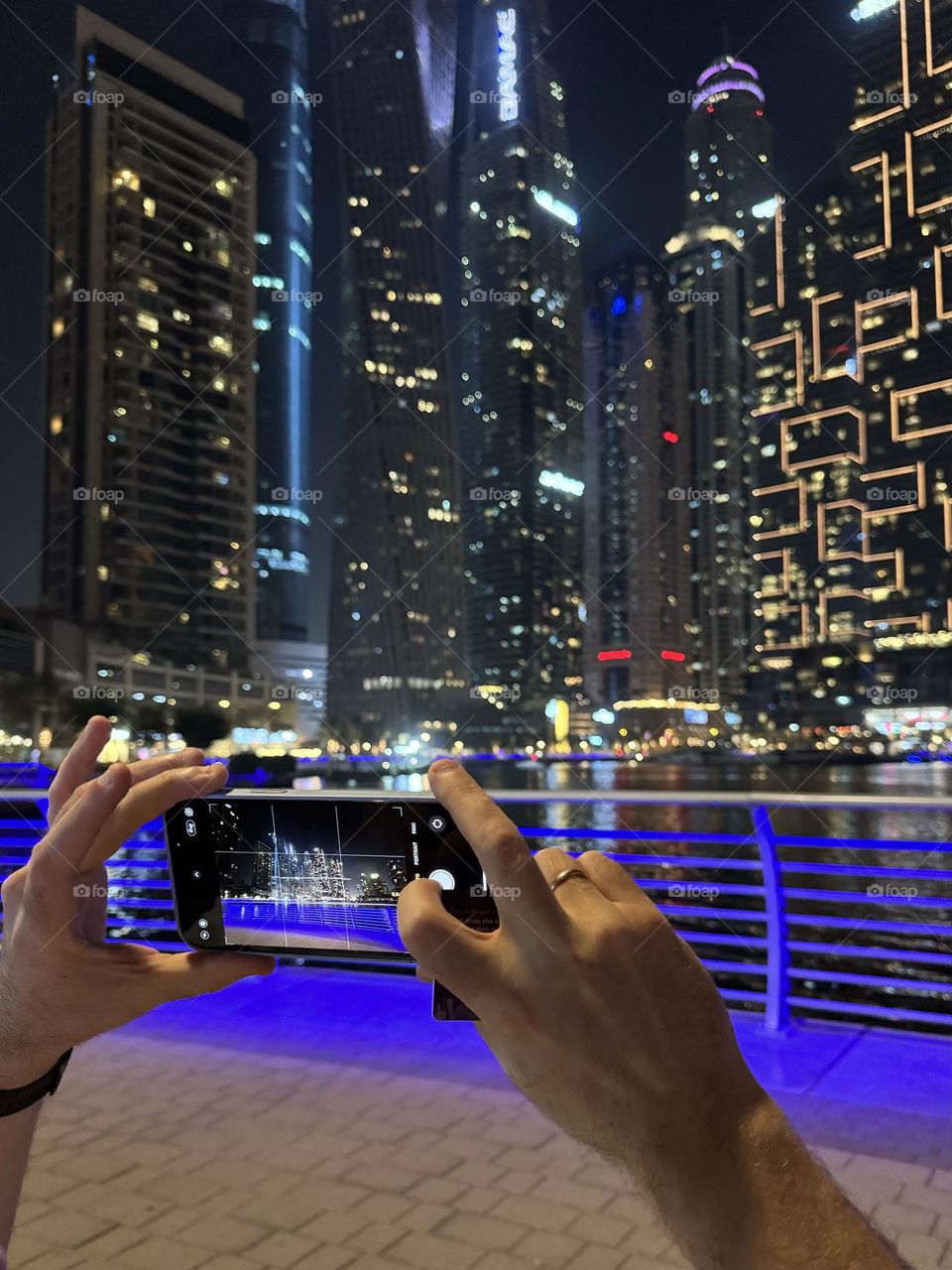 hands holding a phone, a man taking pictures of skyscrapers on his phone in dubai marina