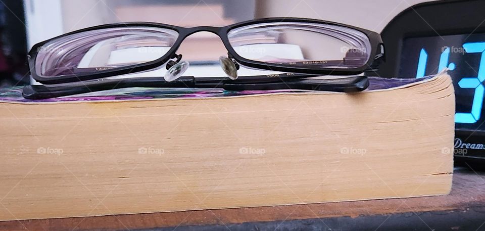 close-up of black glasses on top of closed book by alarm clock toward the end of the day