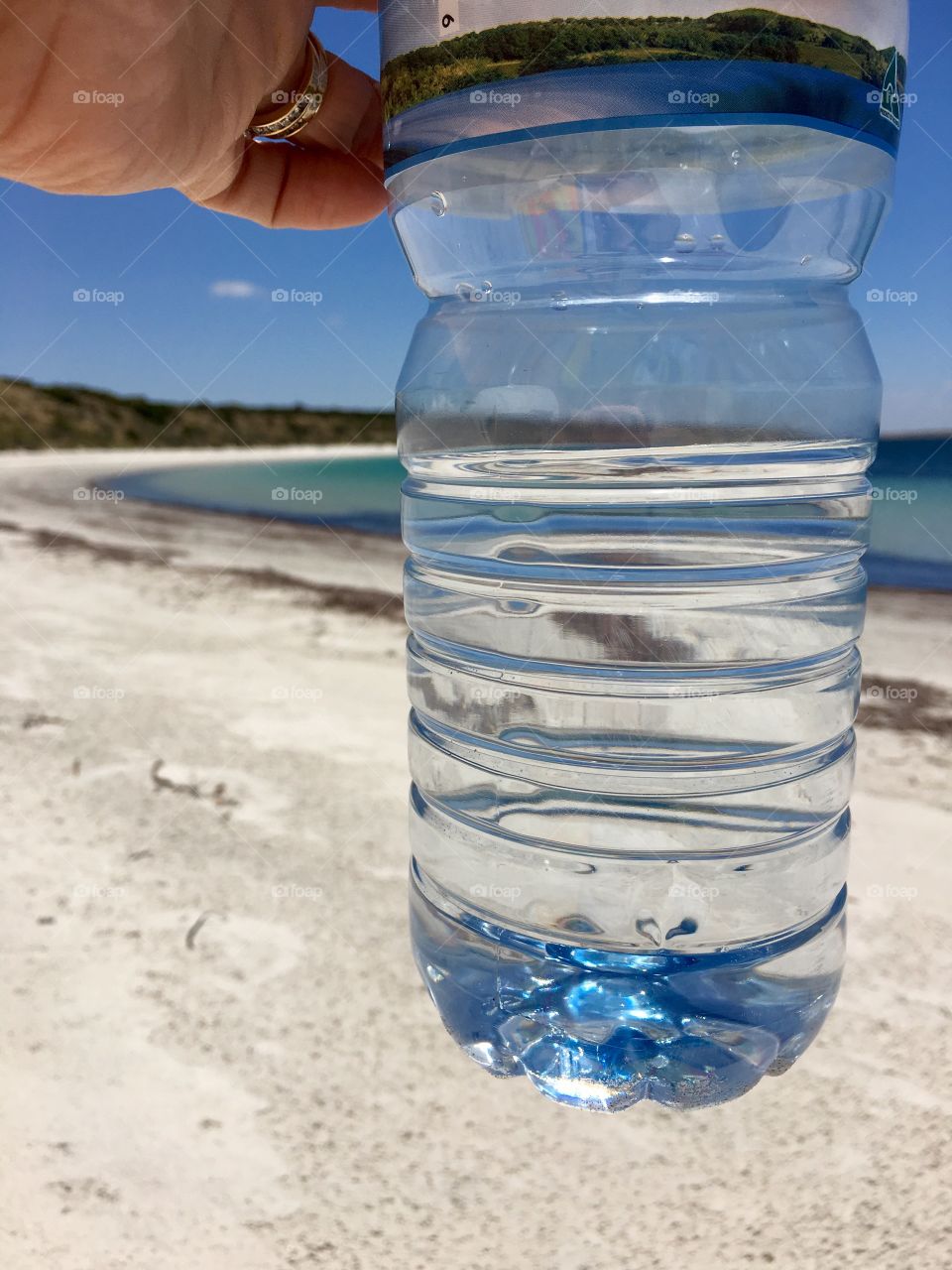 Creative view of the seashore and ocean horizon Brough the perspective of a bottle of pure fresh spring water held by hand of photographer 