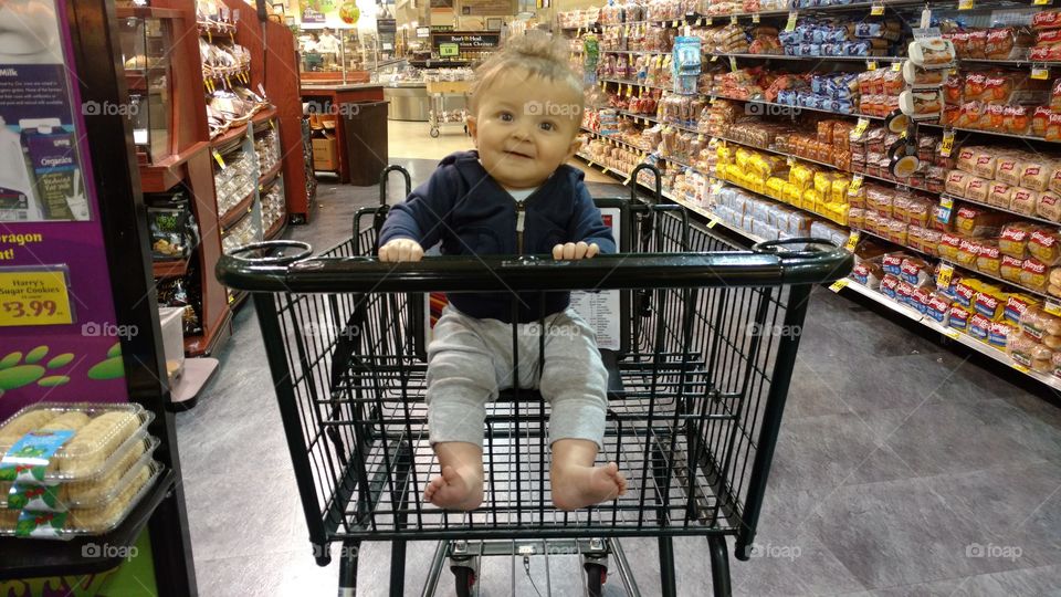An baby boy rides in a shopping cart in the grocery store