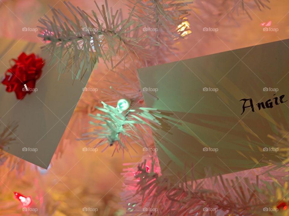 Gift envelopes on a white Christmas tree with soft colored lights. 