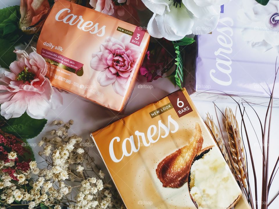 A variety of packs of the new look Caress  bars on a white background accented by complementary florals.