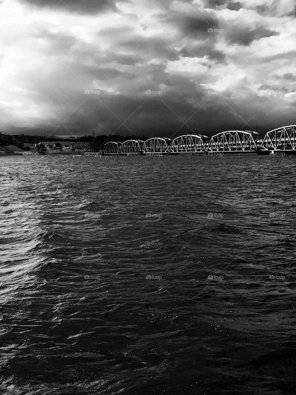 Train bridge and lake with stormy skies. Black and white landscape. 