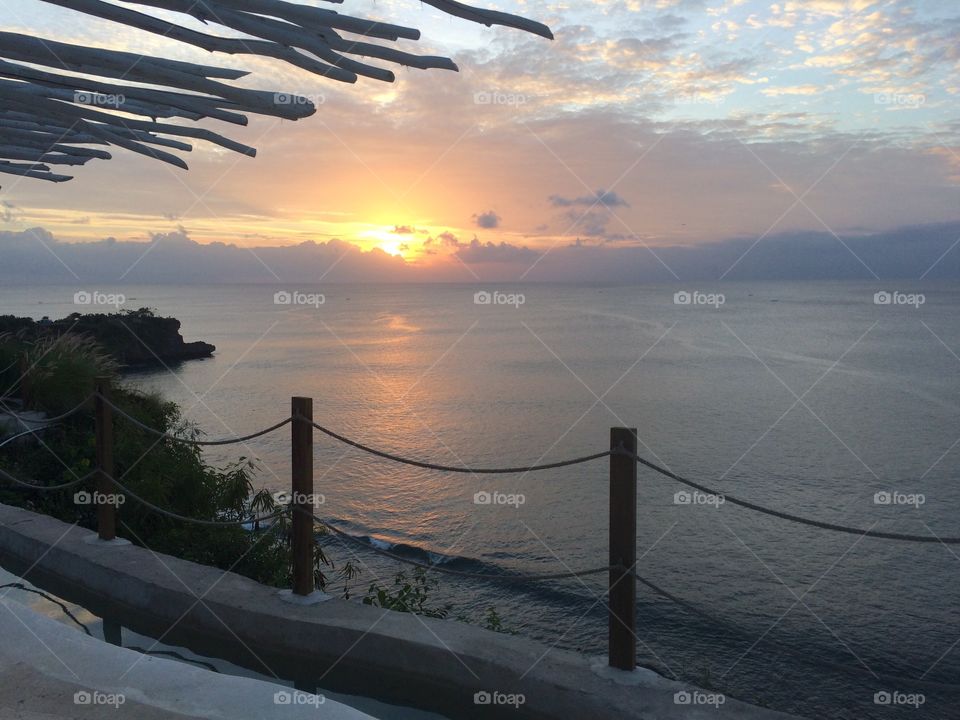 Bali cliffside sunset with roof and fencing in foreground 