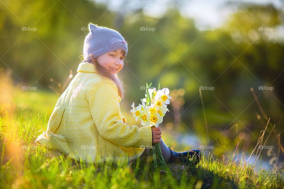 Little girl with narcissus bouquet in spring park.