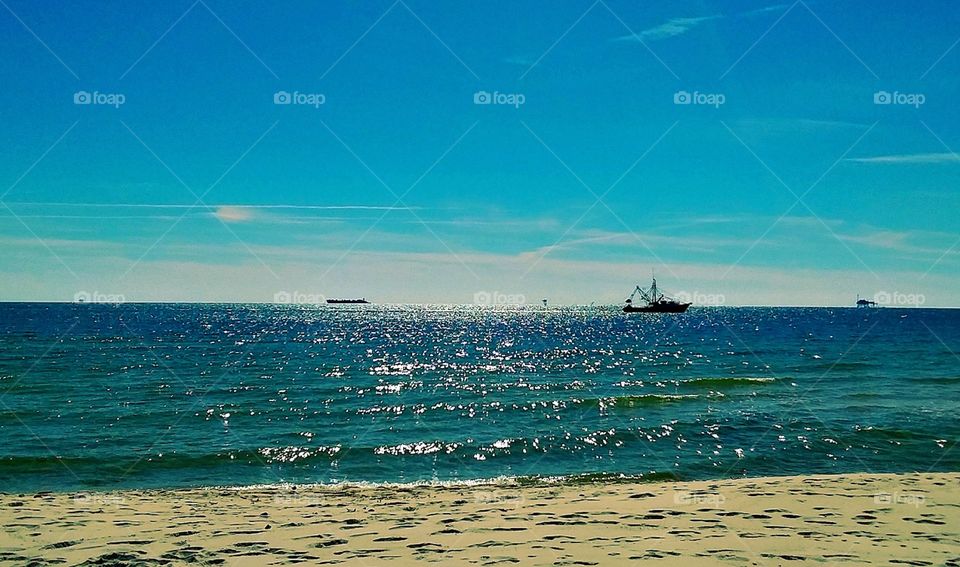 A shrimping boat floating along the coast of the beach on the bright blue glistening ocean