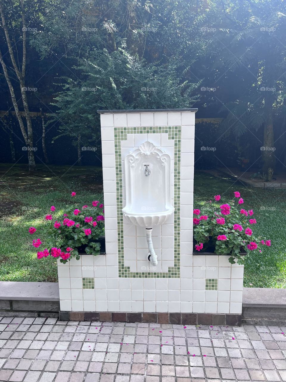 A charming garden fountain adorned with vibrant pink flowers, surrounded by lush vegetation. The elegantly designed white fountain exudes an air of tranquility and harmony, creating an ideal space for relaxation and contemplation