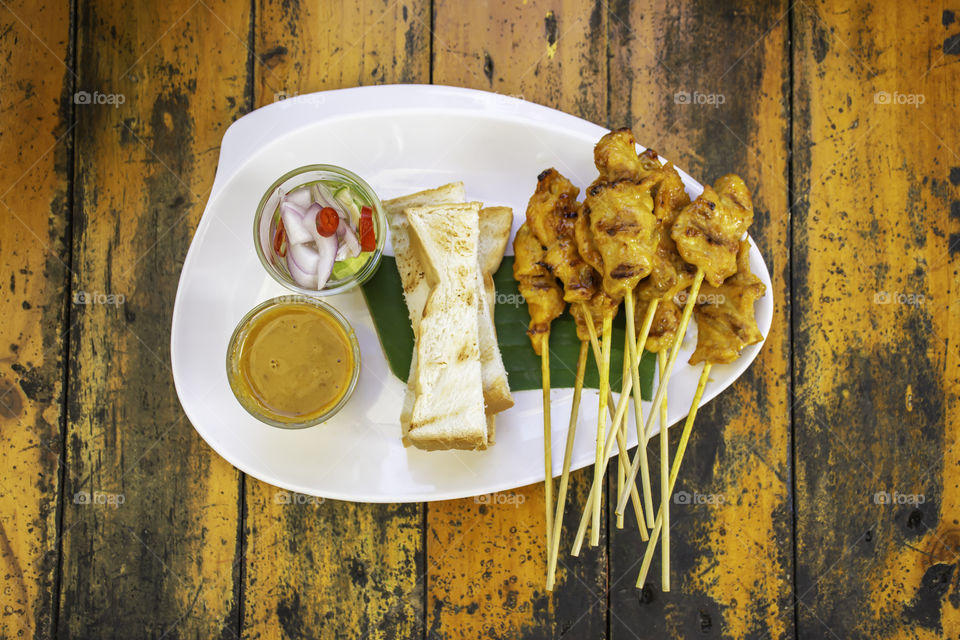 Pork Satay with coconut milk and bread  with sauce in white plastic plate on wooden table.