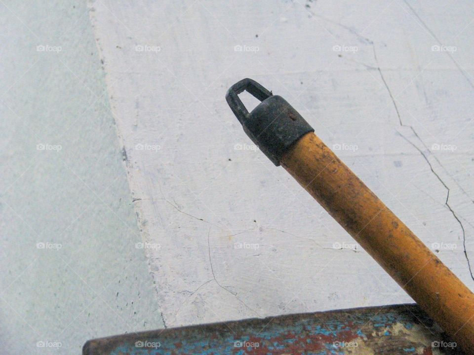 Close-up view of the end of an old broomstick placed against a dull, cracked white wall