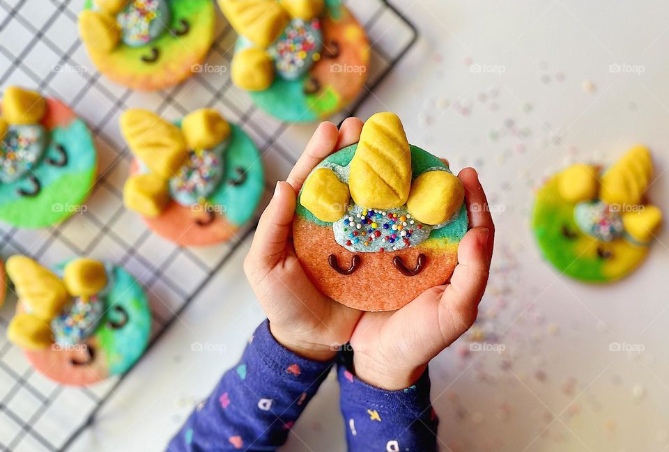 Child holds decorated unicorn sugar cookie, helping mommy make cookies, baking homemade sugar cookies with children, unicorn sugar cookies on display