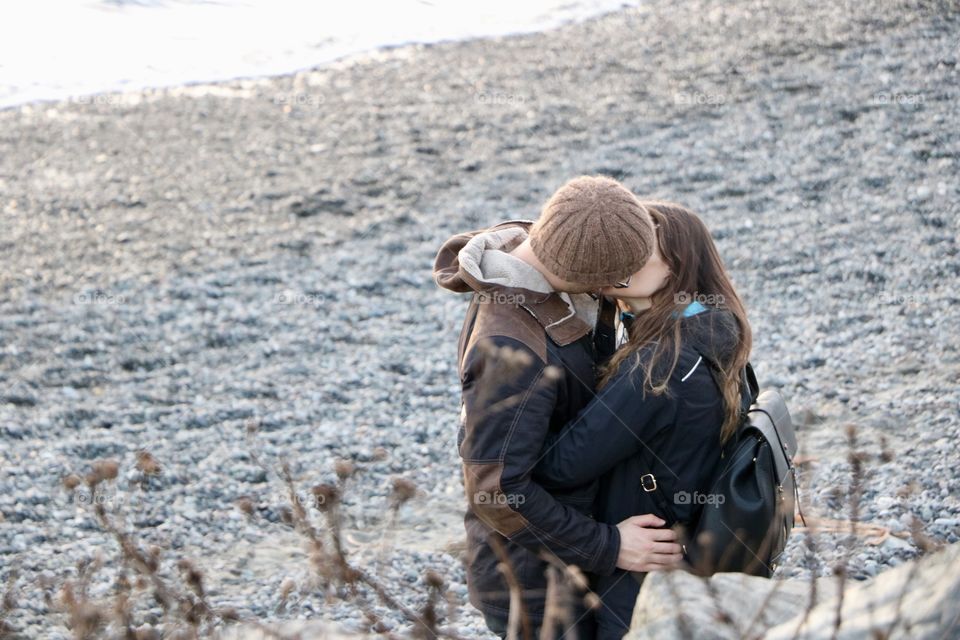 Young couple kissing on  a sandy beach on a winter afternoon..  It is just them at this moment and nothing can spoil this momentum of pure happiness..